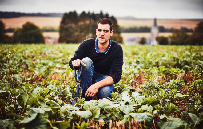 Un homme accroupi dans un champ avec une petite pelle, entouré de plantes